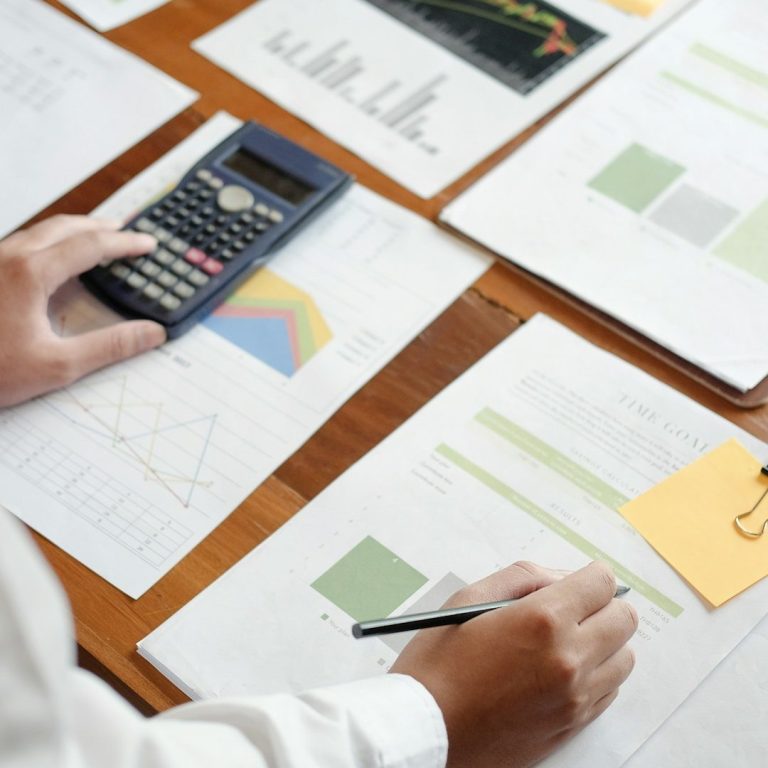Fördermittel berechnen lassen Hände mit Taschenrechner und Stift auf Diagramme und Statistiken auf einem Tisch.